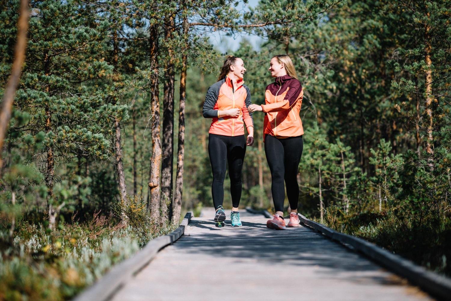 Ystävykset kävelemässä Paukanevan pitkospuilla nauraen.