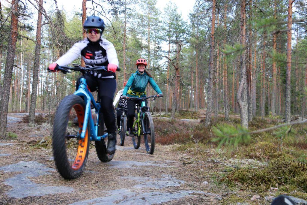 Maastopyöräilijät kulkevat peräkkäin kallioisessa metsämaastossa