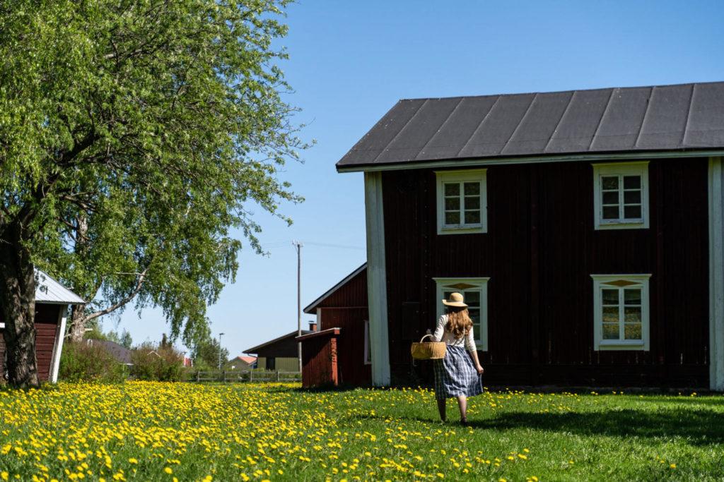 Nainen kävelee pohjalaisrakennuksen pihamaalla eväskori kädessä