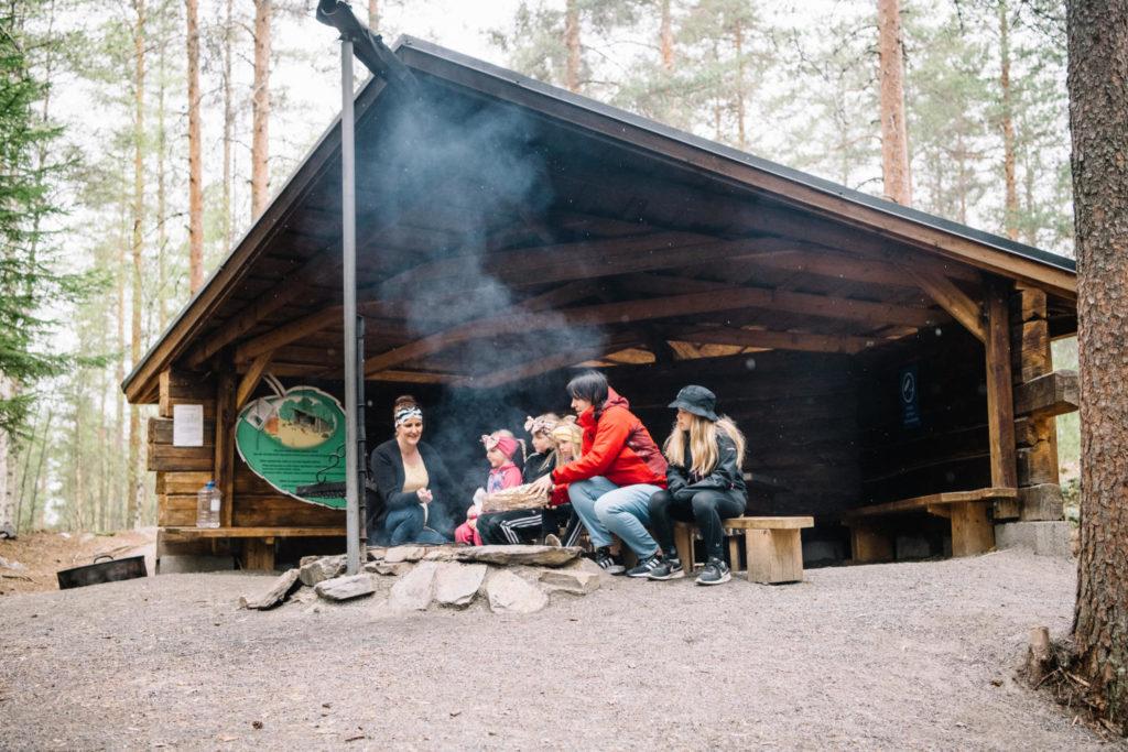 Perhe sytyttää nuotiota lastenreitin laavun nuotiopaikalla.