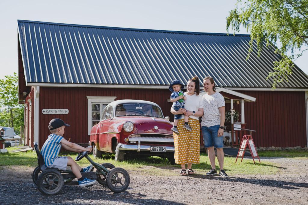 Poika ajaa polkuautolla Wanhan Markin pihassa perheen katsoessa vierestä