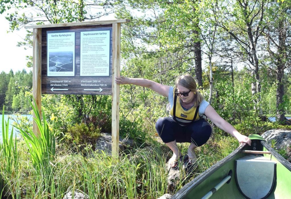 Meloja kiipeää kajakkia kohden pitäen kiinni kyltistä ja kajakista