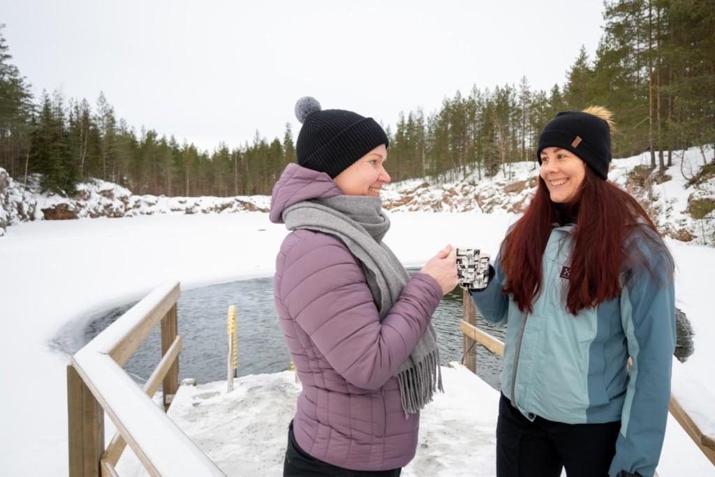 Naiset toppavaatteissa kahvikuppi kädessä avannon vieressä