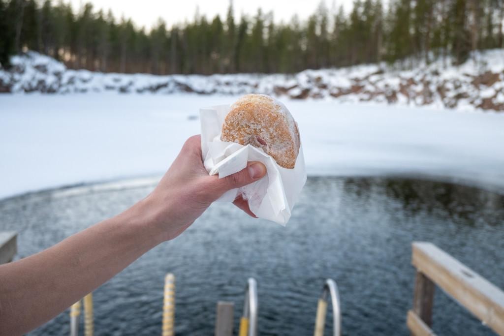 Naisen käsi pitelee munkkia avannon vieressä