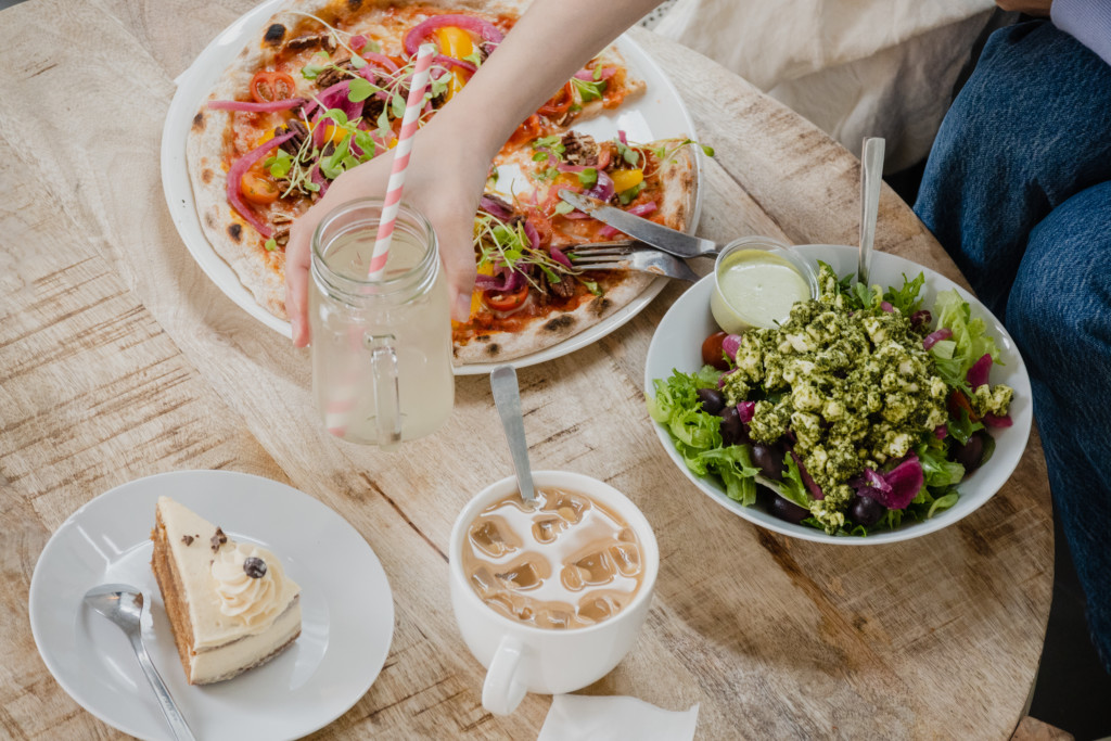 Pöydällä vegaaninen pizza, salaattia ja vegaanista kakkua 