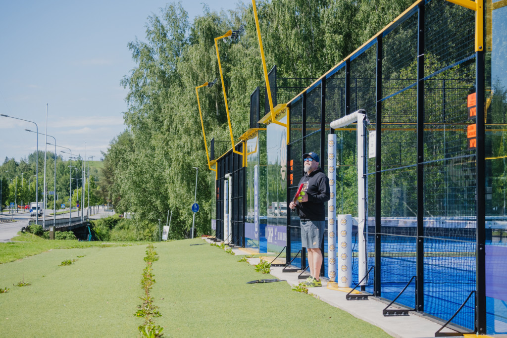 Mies seisoo ulkona padel pelikentän vierellä kesällä