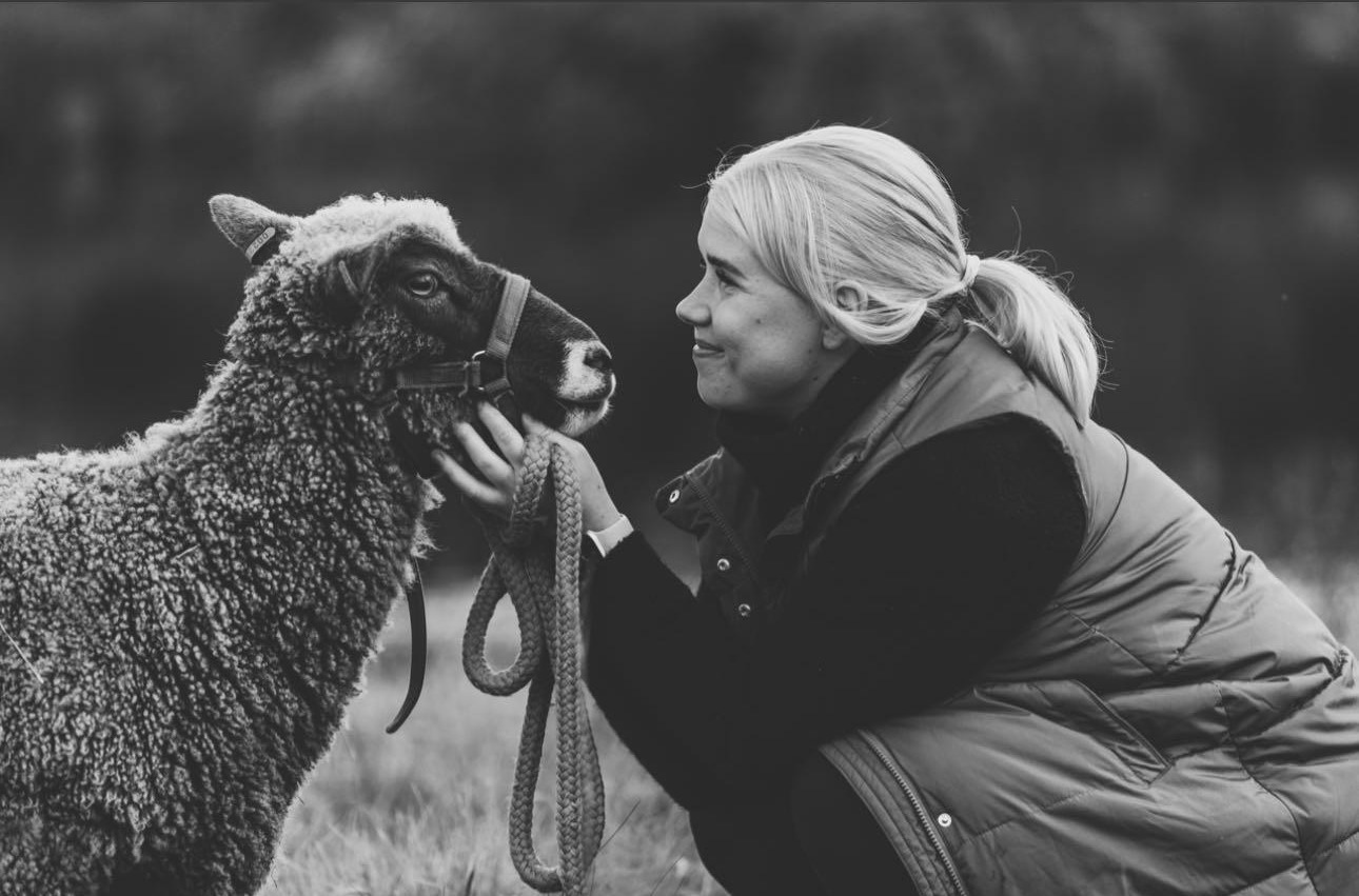 Nainen pitelee hymyillen lampaasta kiinni